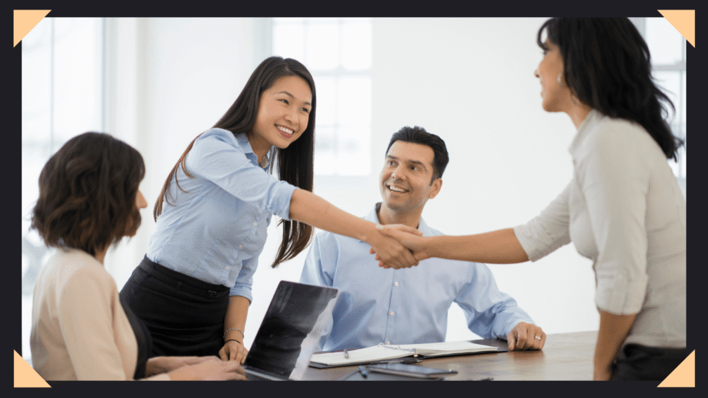 Woman shaking hands with a new client while sitting at the conference table with others.